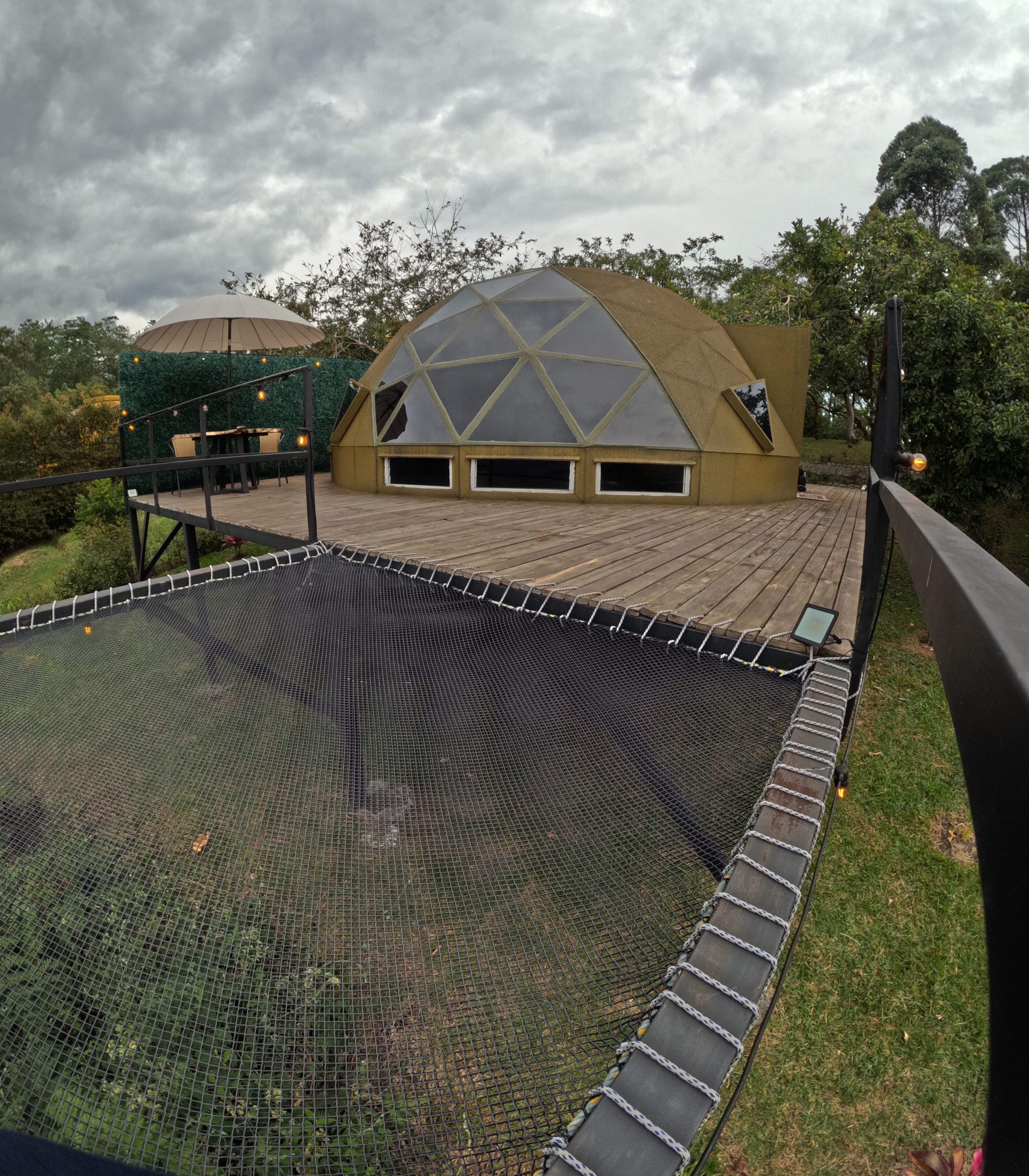 A geodesic dome structure with a wooden deck and a netted trampoline area.
