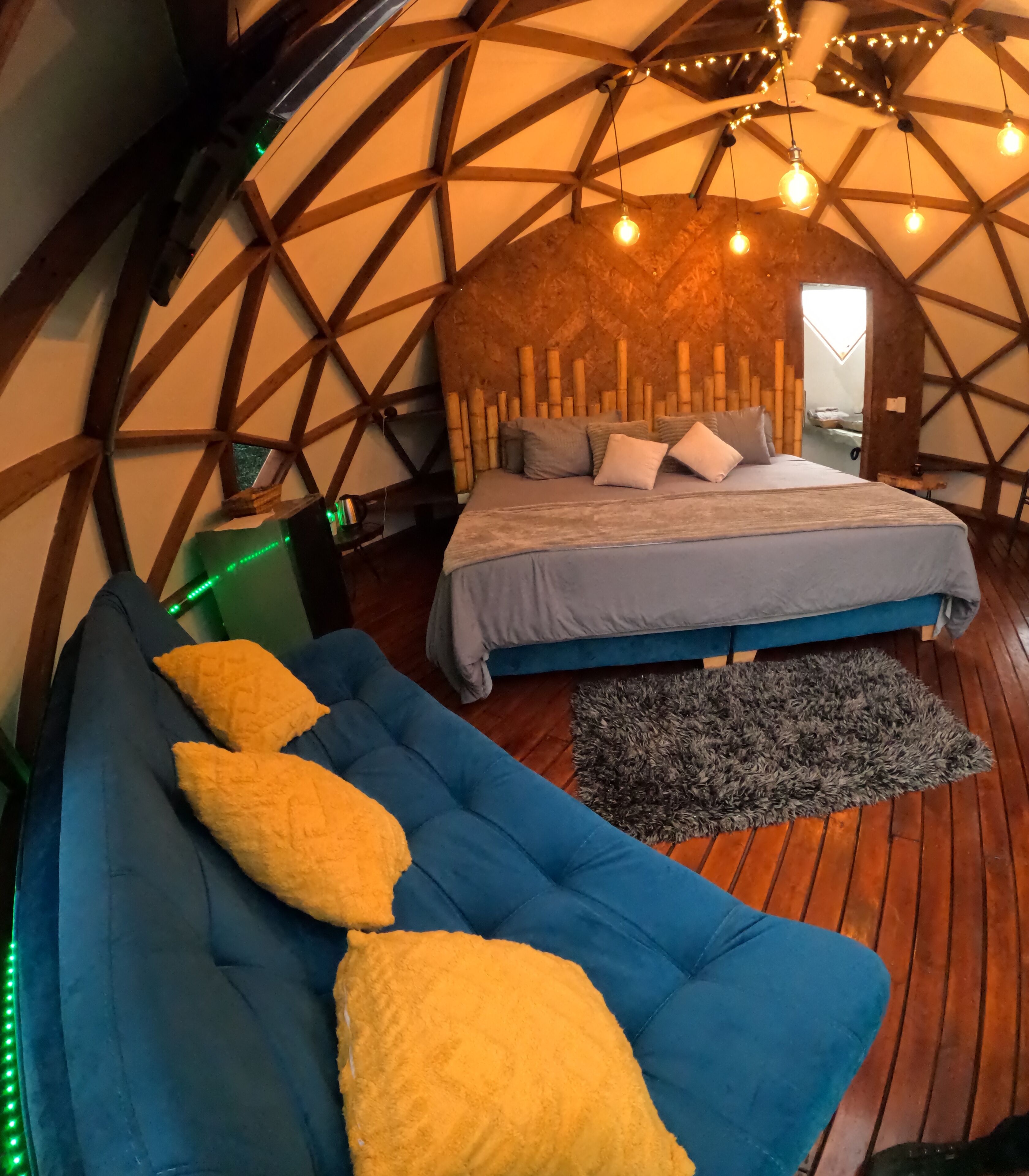 Una habitación acogedora con una cama, un sofá azul con cojines amarillos y suelo de madera.