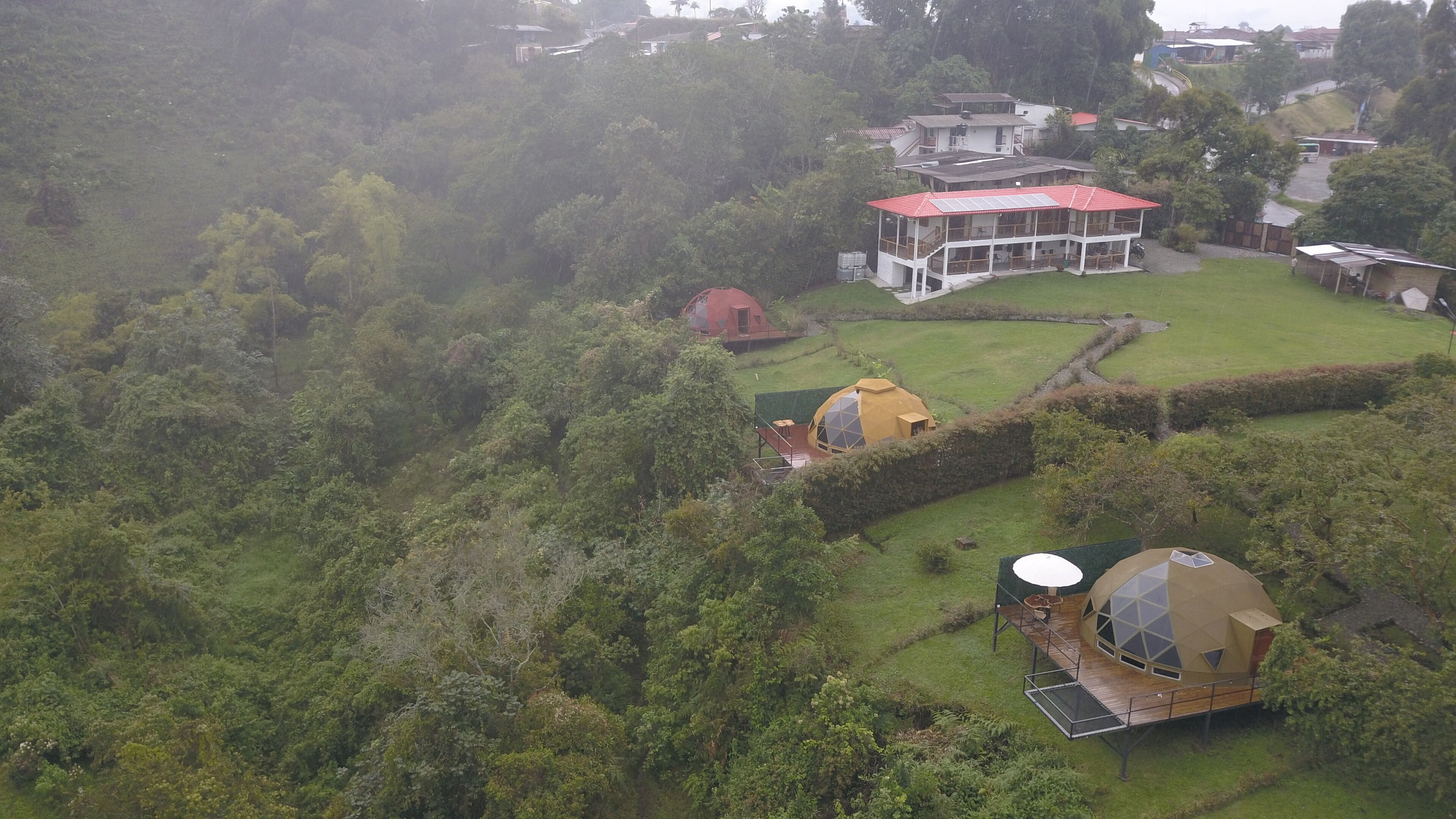 A large house with a red roof and multiple rooms, surrounded by lush greenery and a small garden.