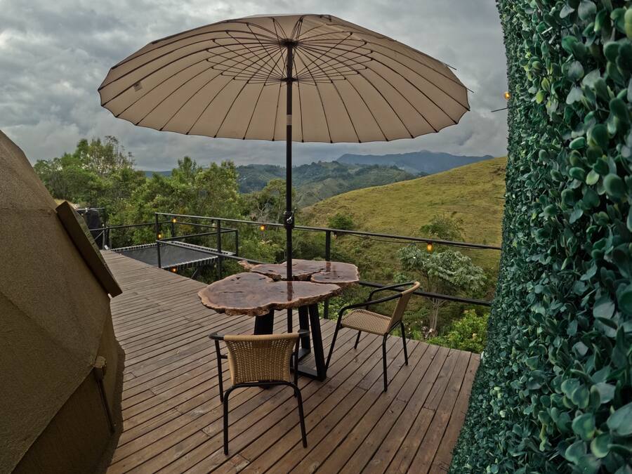 Una terraza de madera con una mesa, sillas y una sombrilla, con vistas a las colinas.