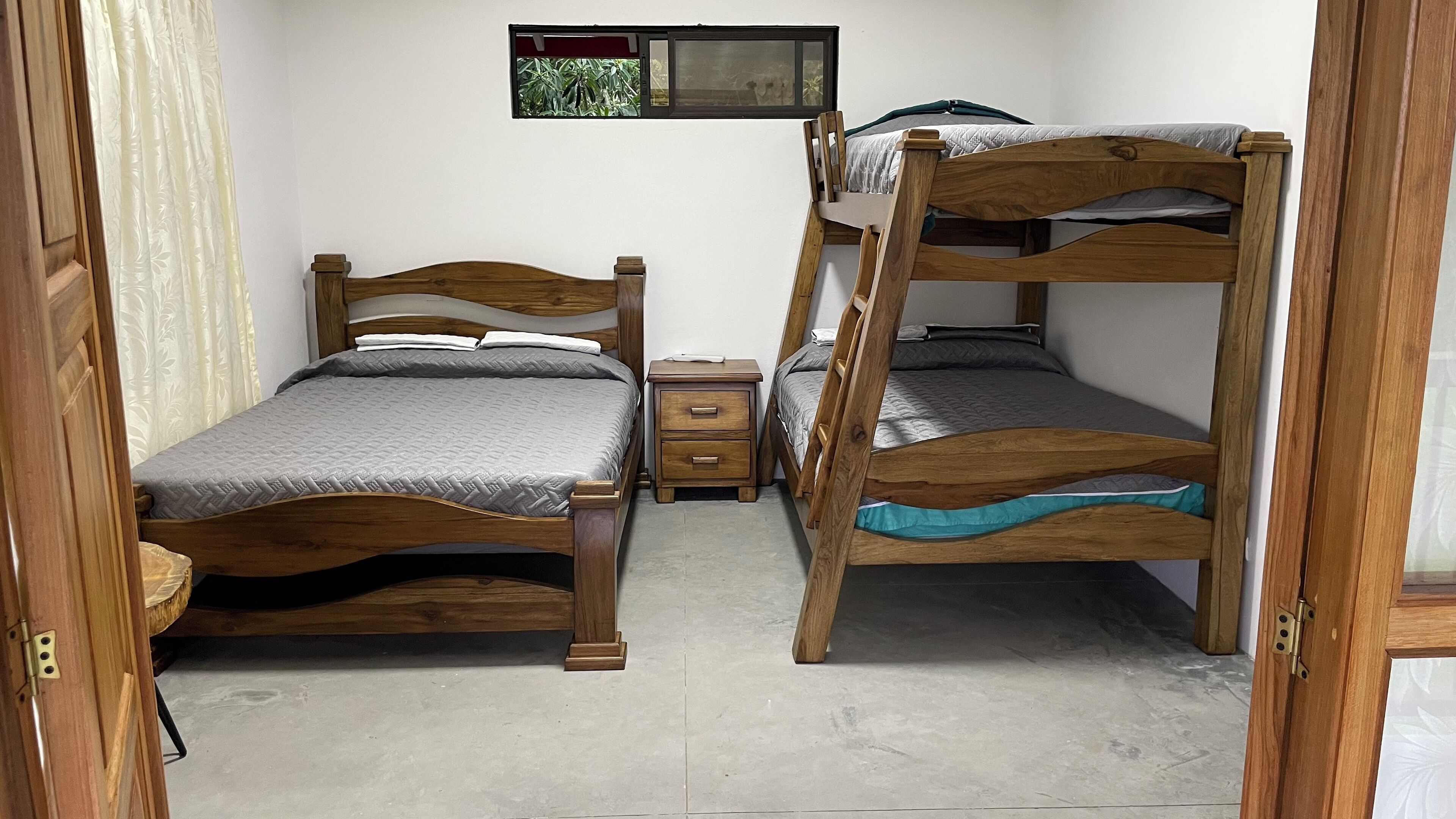 Una habitación con dos camas literas de madera, una mesita de noche pequeña y una ventana con vistas a zonas verdes.