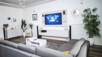 A modern living room with a grey sofa, white entertainment unit, and a flat-screen TV mounted on the wall.