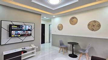 A modern waiting area with a flat-screen TV mounted on the wall, two grey chairs, a small round table, and decorative wall art.