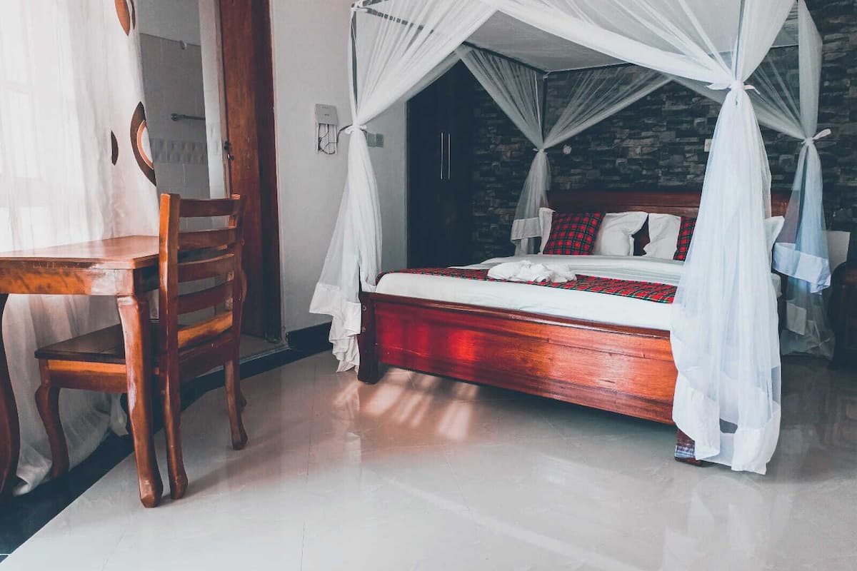 Quarto com cama de madeira, dossel branco e colcha xadrez vermelha e preta.