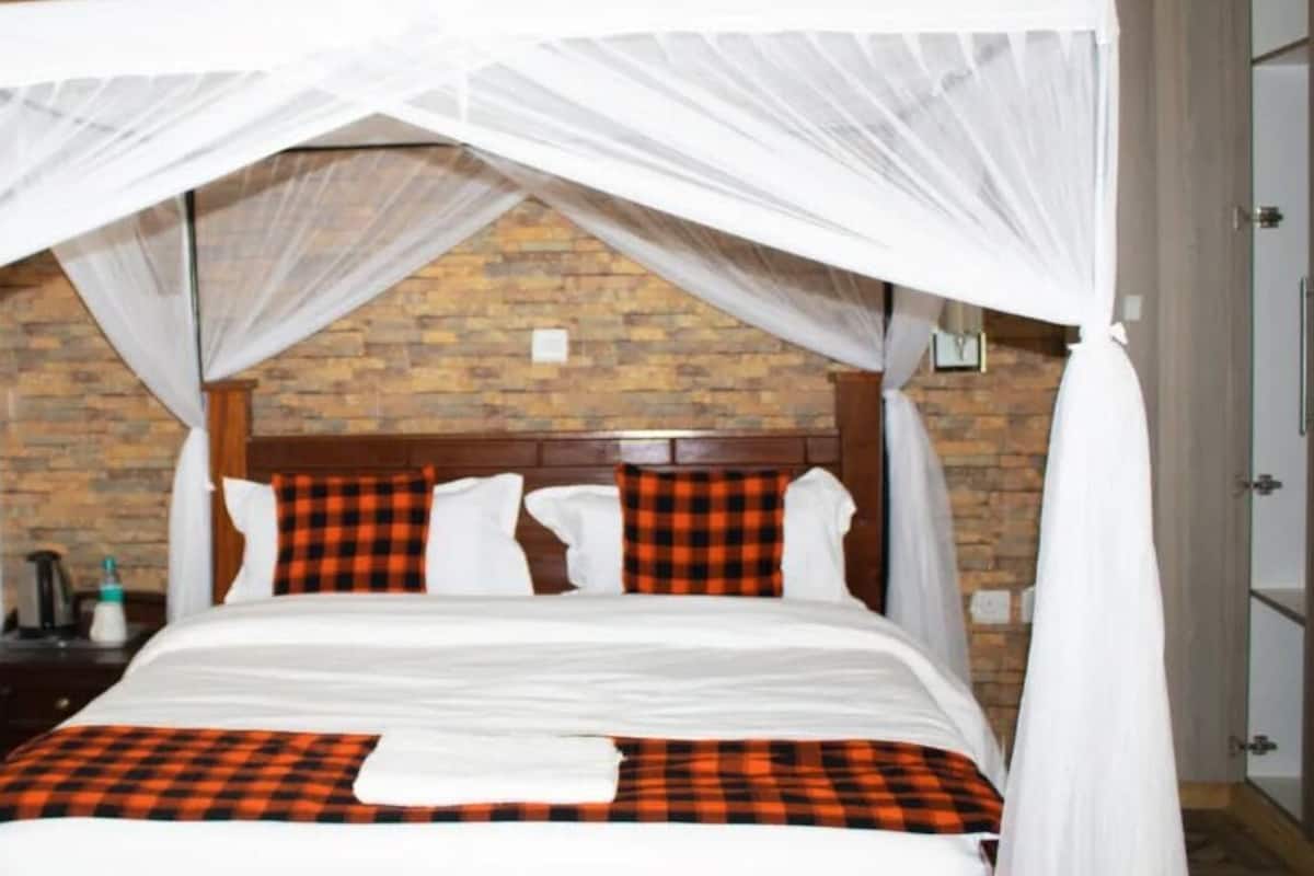 Uma cama com dossel branco e roupa de cama xadrez, parede de tijolos ao fundo e cabeceira de madeira.