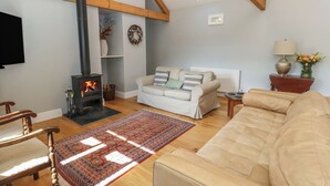 A cozy living room with a fireplace, a sofa, a chair, and a wooden floor. - Bower Cottage (Beaminster)