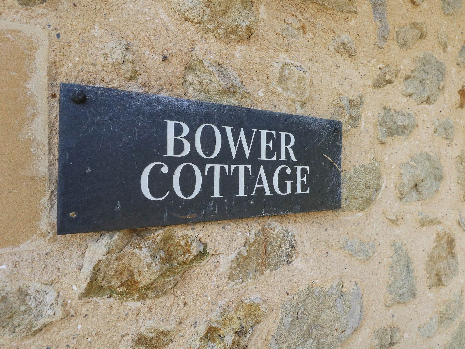 Eine Steinsäule mit einem schwarzen Schild, auf dem 'BOWER COTTAGE' steht.