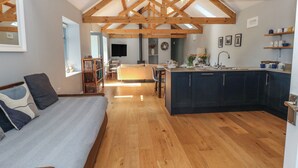 A spacious living area with a wooden ceiling, a kitchen with dark cabinets, and a cozy seating area with a sofa and pillows. - Bower Cottage (Beaminster)