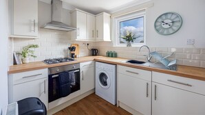 A compact kitchen with white cabinets, a stove, a washing machine, and a window with a view of the sky.