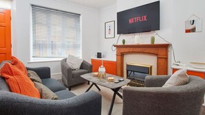 En moderne stue med pejs, et fladskærms-tv monteret over den, og et hyggeligt siddeområde med to sofaer og et sofabord.