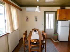 Zona pranzo con tavolo in legno, sedie, una ventola a soffitto bianca, un frigorifero bianco e una finestra con tende.