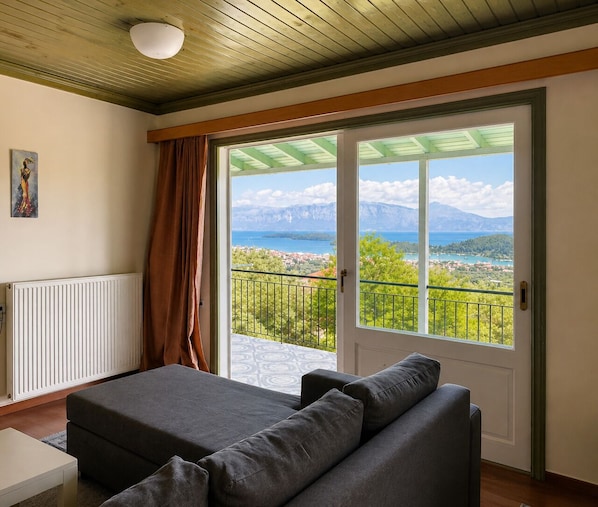 Ein Zimmer mit Bett, Heizkörper, einem Bild und einem Balkon mit Blick auf Berge und Meer.