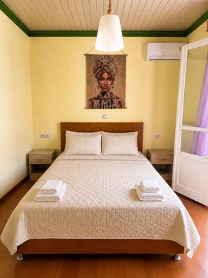 Un dormitorio con una cama, dos mesitas de noche, un cuadro en la pared y un equipo de aire acondicionado.