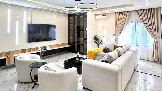 A modern living room with a flat-screen TV, a sofa, a coffee table, and a seating area with a plant. - Winnie Host and Homes (Abuja)