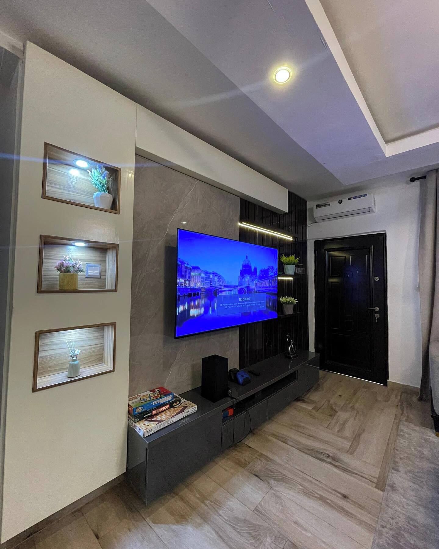 A modern living room with a flat-screen TV mounted on the wall, a dark entertainment unit, and a wooden floor.