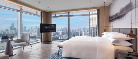 Habitación de hotel moderna con una cama grande, televisión, escritorio y vistas a la silueta urbana.