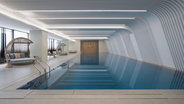 A modern indoor swimming pool with a glass barrier, seating area with lounge chairs, and a curved ceiling design. - Courtyard By Marriott Guangzhou Pazhou (Guangzhou)