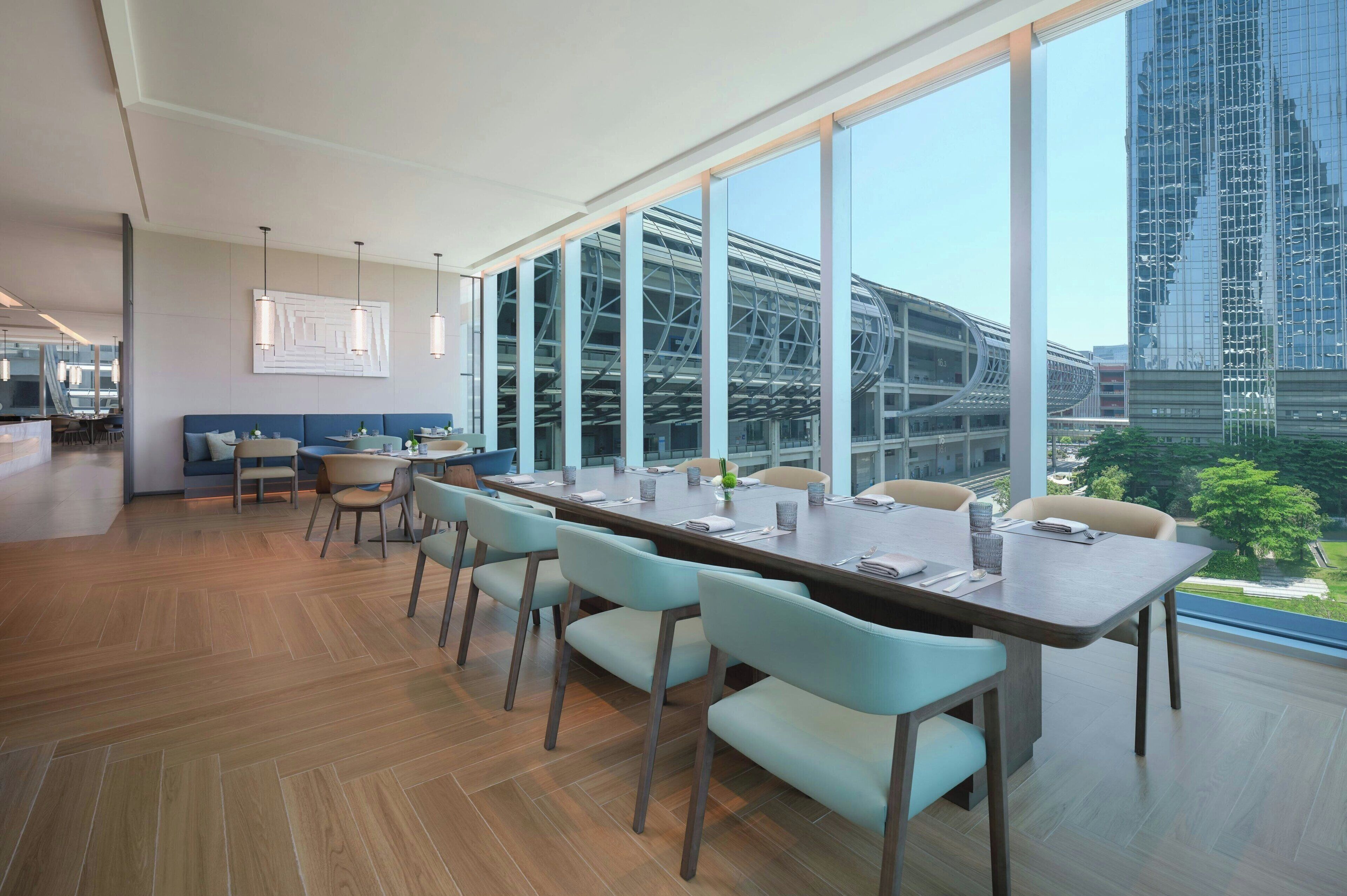 A modern conference room with a long table, chairs, and large windows offering a view of a cityscape and a bridge.