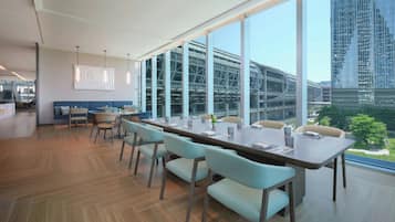 A modern conference room with a long table, chairs, and large windows offering a view of a cityscape and a bridge.