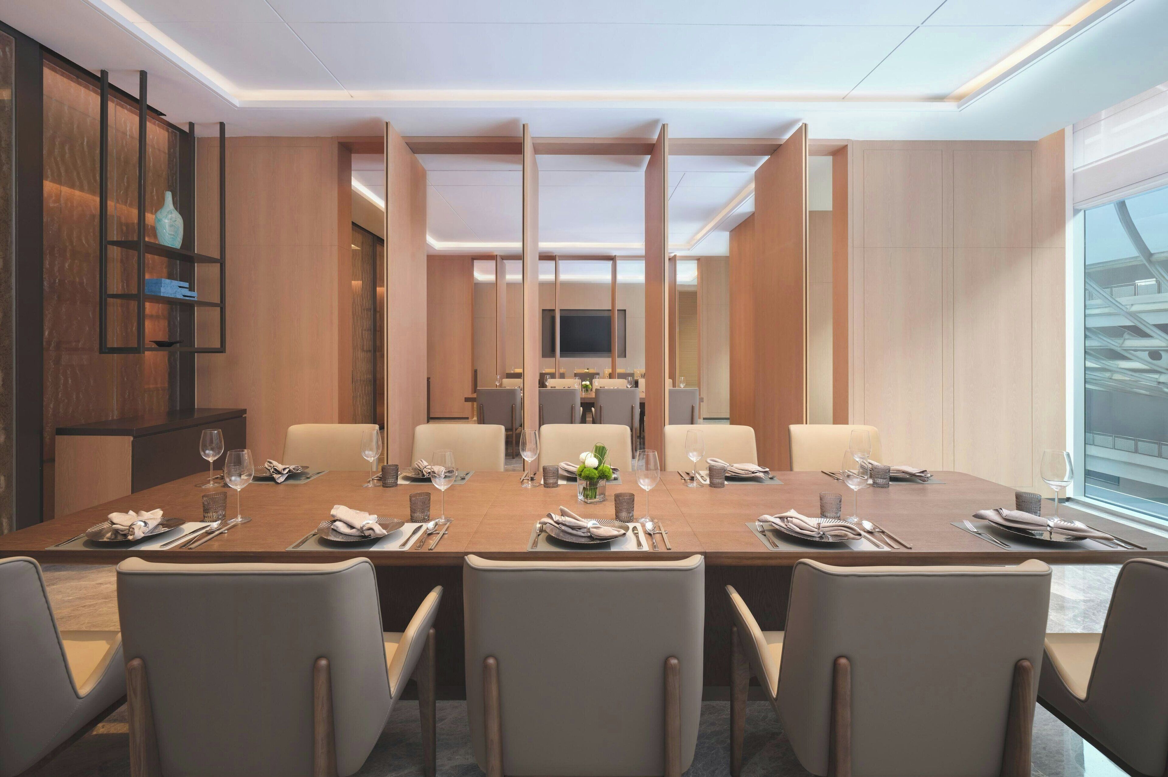 A modern conference room with a long table, comfortable chairs, and a large screen at the front.