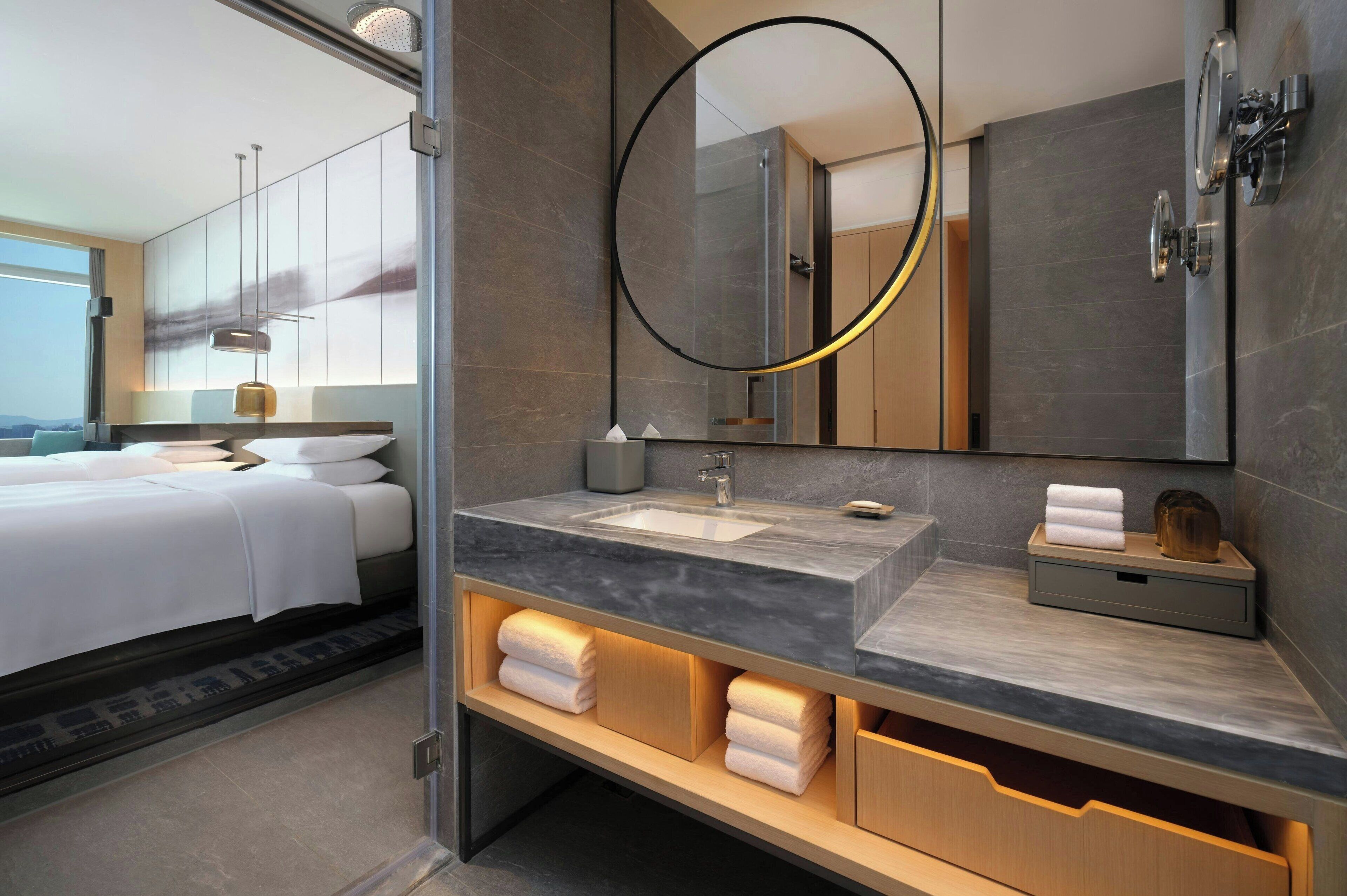 Un baño de hotel moderno con un espejo grande, un lavamanos y un mueble tocador con espacio de almacenamiento.