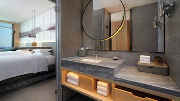 Un baño de hotel moderno con un espejo grande, un lavamanos y un mueble tocador con espacio de almacenamiento.