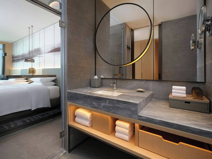 Un baño de hotel moderno con un espejo grande, un lavamanos y un mueble tocador con espacio de almacenamiento.