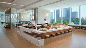 A modern kitchen with chefs preparing food, large windows with city views, and a marble countertop with various dishes. - Courtyard By Marriott Guangzhou Pazhou (Guangzhou)