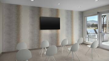 A conference room with a flat-screen TV mounted on the wall, surrounded by white chairs with metal legs.