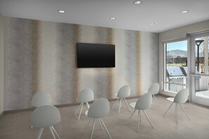 Een vergaderruimte met een flatscreen televisie aan de wand, omringd door witte stoelen met metalen poten.
