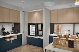 Una cocina moderna con una máquina para gofres, bebidas refrigeradas y frascos con nueces y frutas secas.