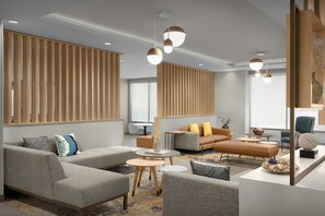 Un salon moderne avec des canapés gris, un canapé marron agrémenté de coussins jaunes, une table basse et un vase décoratif.