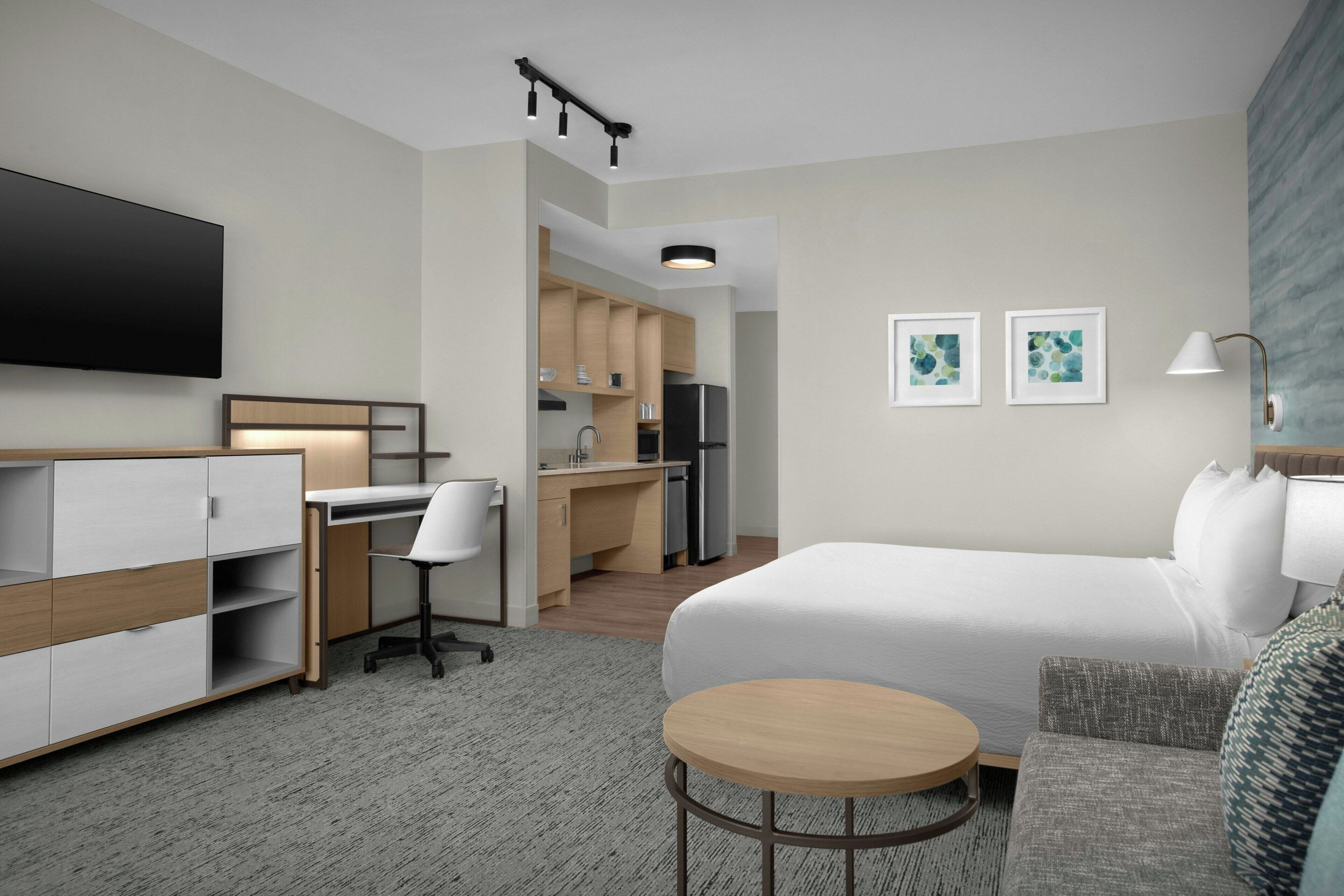 Une chambre d’hôtel moderne équipée d’un lit, d’un bureau, d’une chaise et d’une kitchenette.