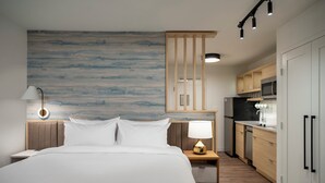 A hotel room with a bed, bedside lamp, wall art, a kitchen area with appliances, and a wooden cabinet. - Towneplace Suites By Marriott Palmdale (Palmdale)