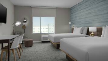 A hotel room with two beds, a desk, chairs, a TV, and a large window.