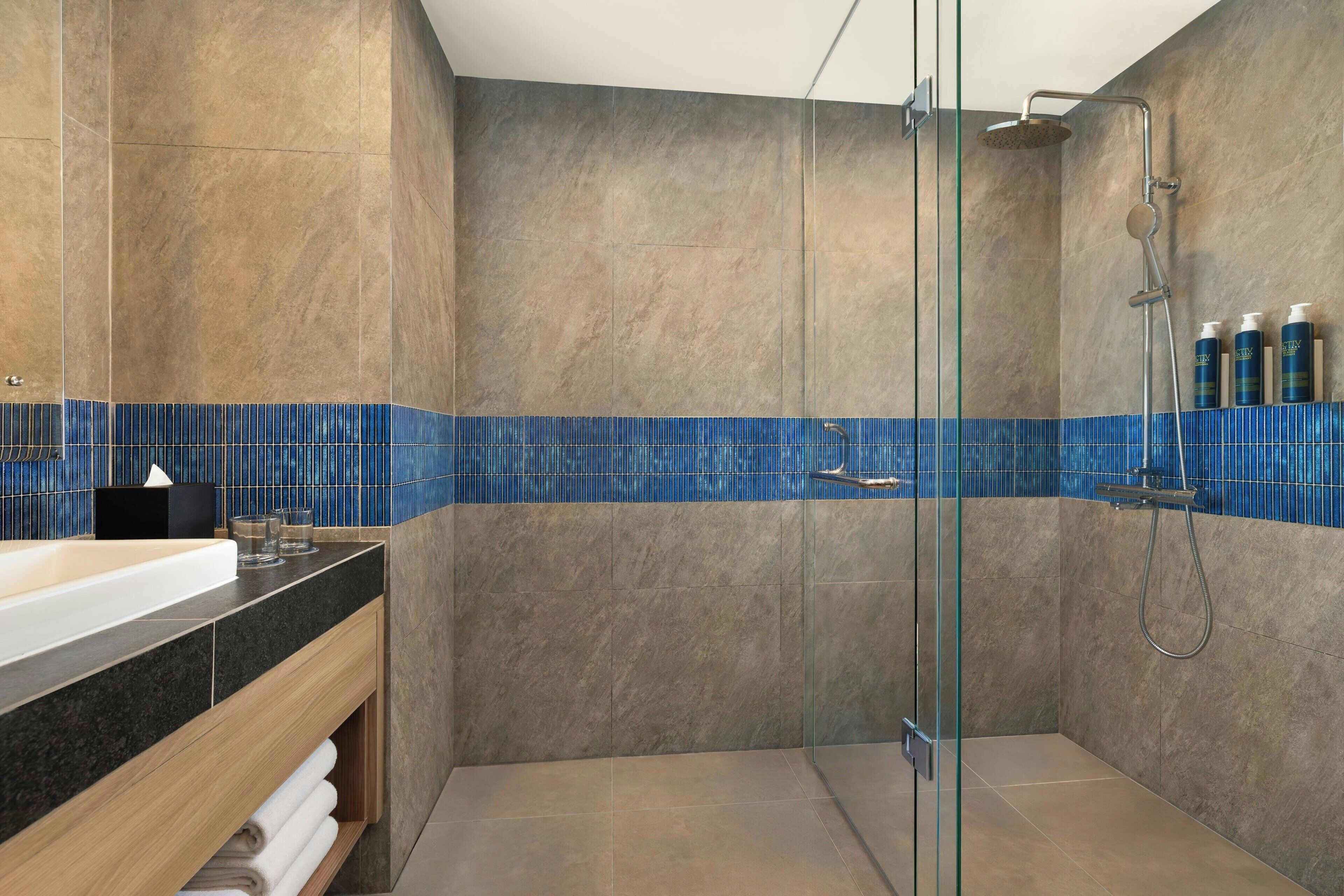 A modern bathroom with a glass-enclosed shower, a wooden vanity, and a blue-tiled backsplash.