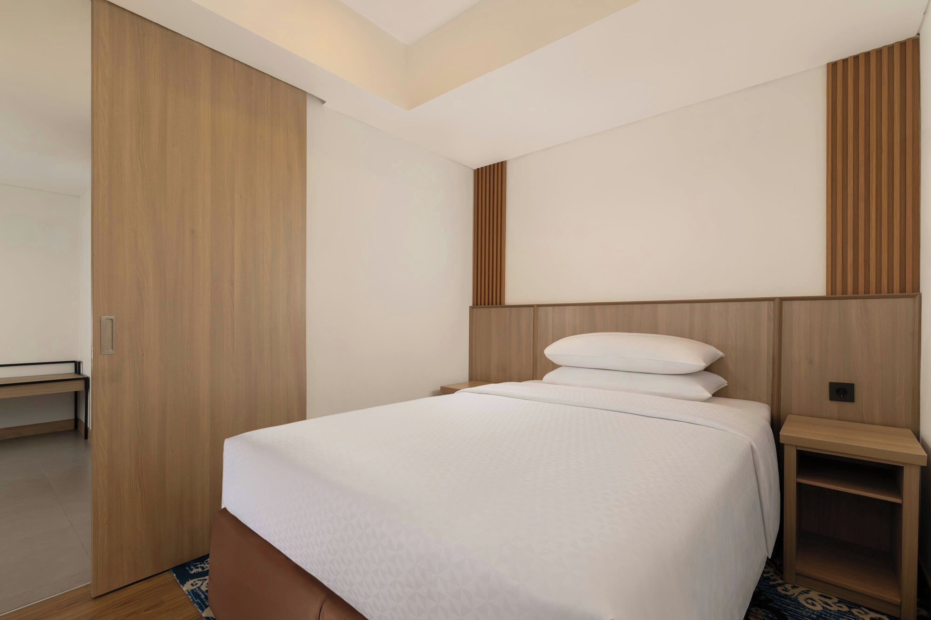 A hotel room with a bed, a wooden wardrobe, a bedside table, and a bench.