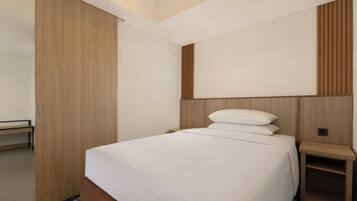 A hotel room with a bed, a wooden wardrobe, a bedside table, and a bench.