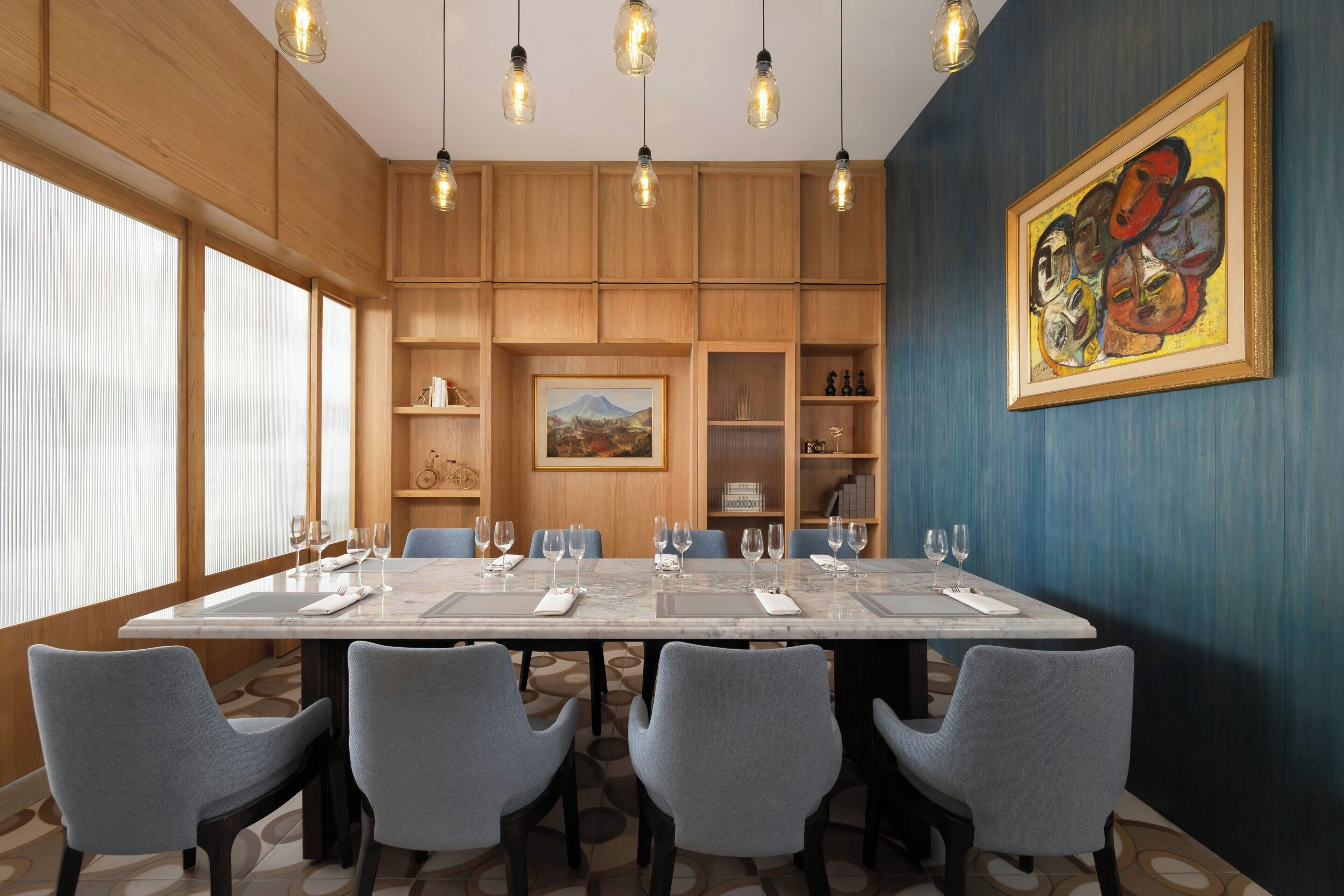 A conference room with a long table, six chairs, and a painting on the wall.