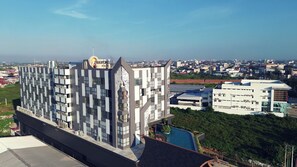 Un hôtel à plusieurs étages doté d’une architecture moderne, caractérisé par une tour centrale imposante et une piscine sur le toit.