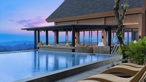 A poolside area with a bar, lounge chairs, and a view of the mountains. - Four Points By Sheraton Pontianak (Pontianak)