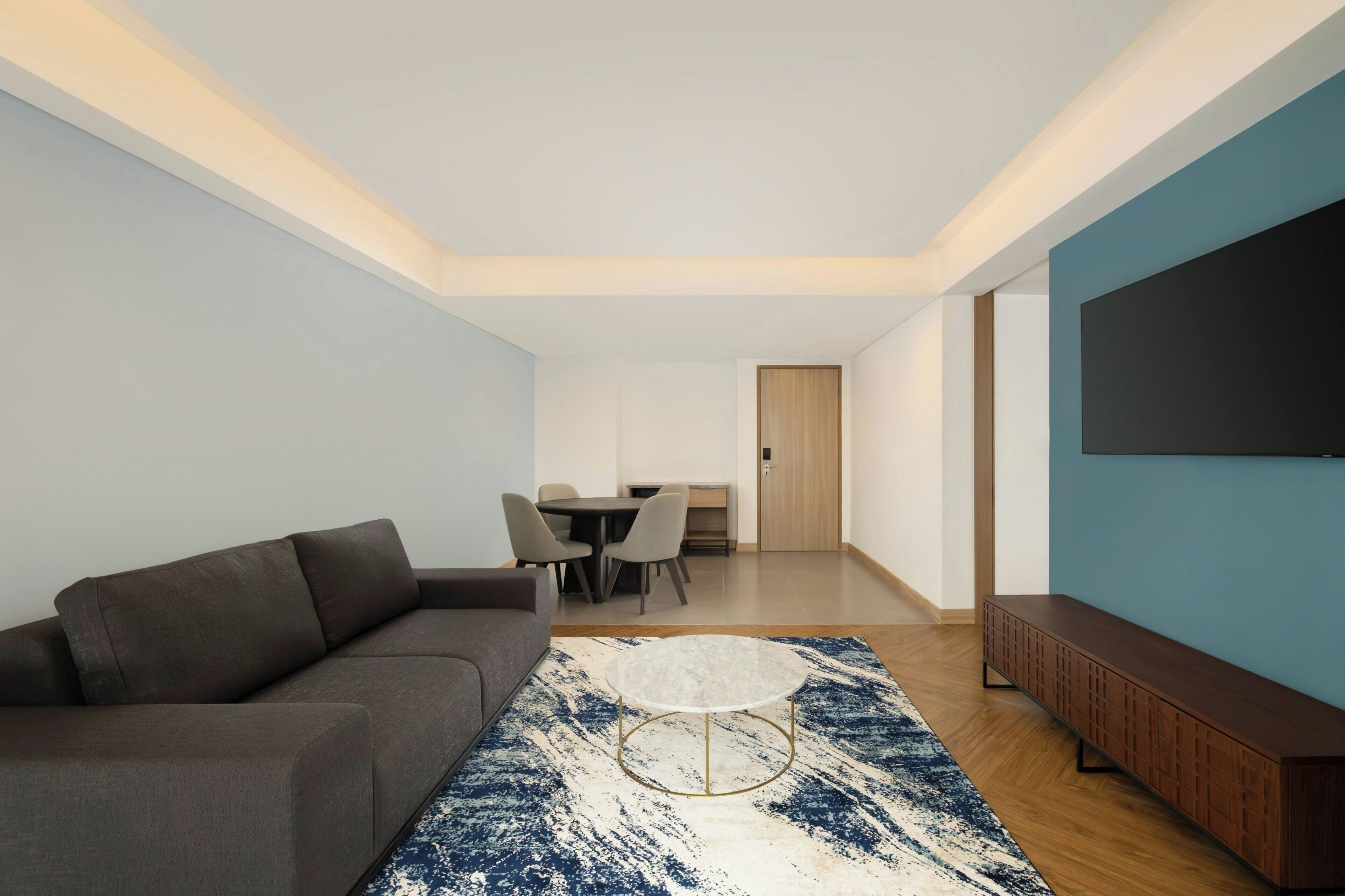 Una sala moderna con un sofá, una mesa redonda de centro, una zona de comedor con sillas y un televisor montado en la pared.