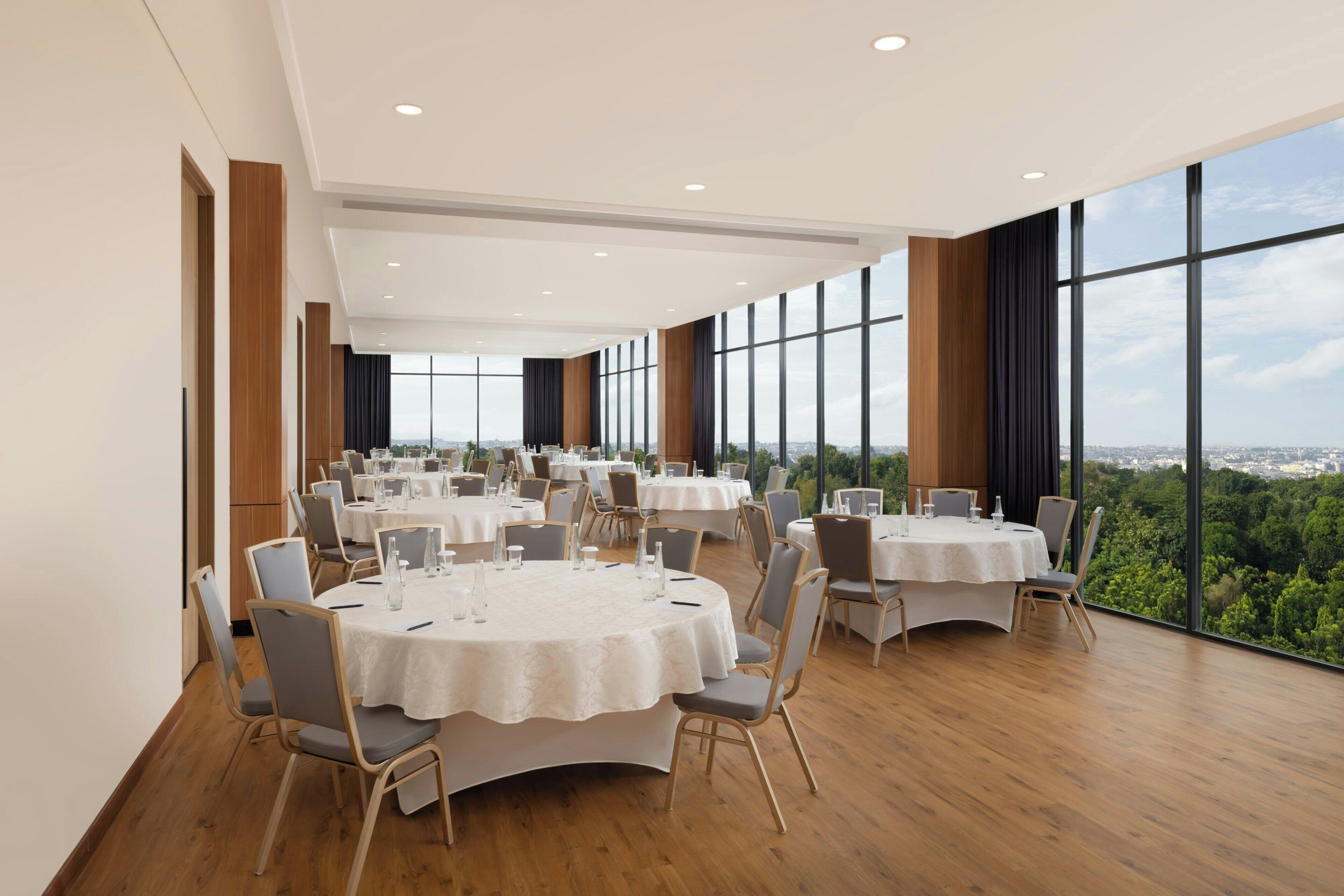 Uma sala de conferência ampla, com várias mesas e cadeiras, e janelas grandes que oferecem vista para a cidade.