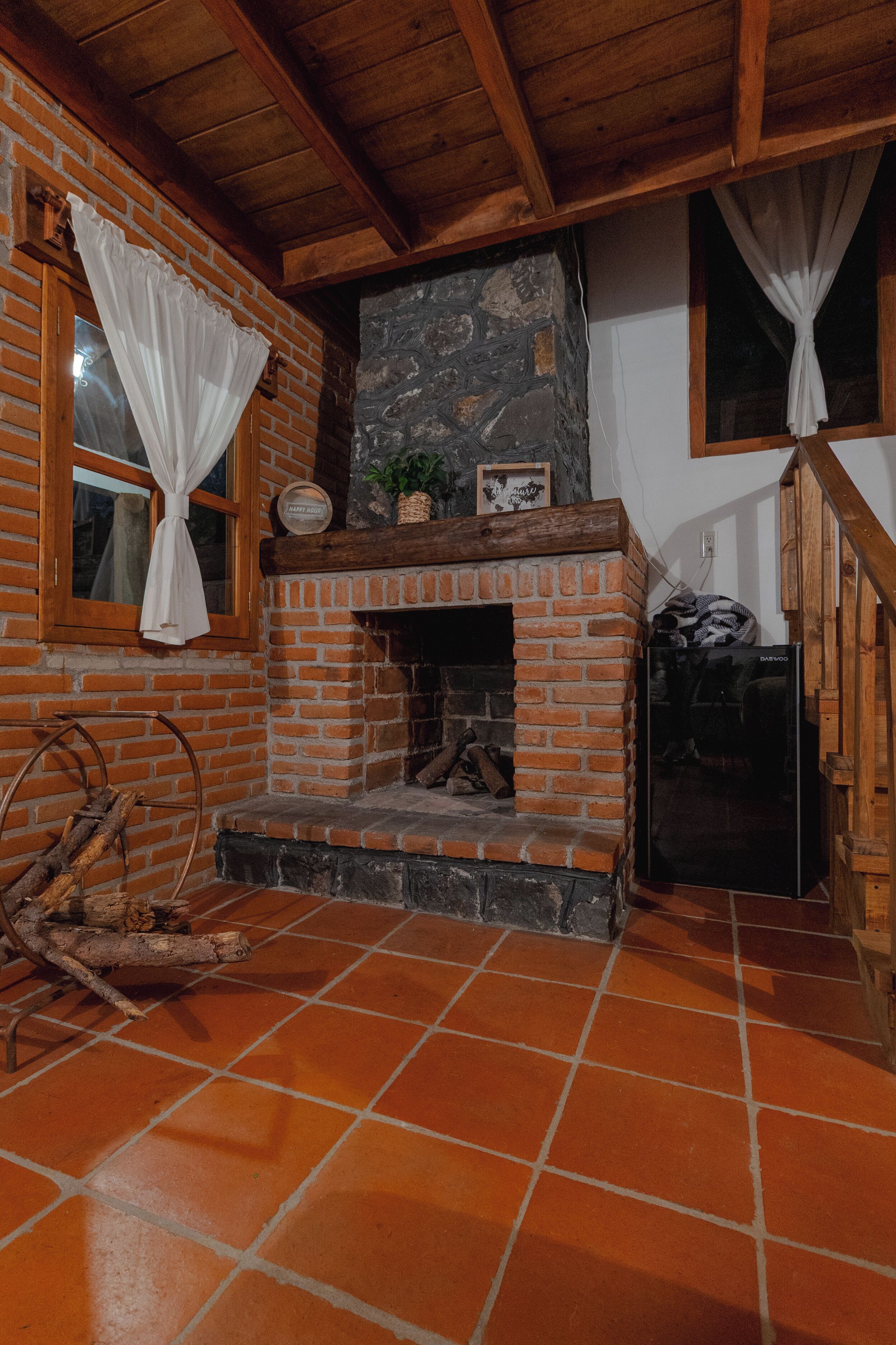 A rustic room with a brick fireplace, wooden beams, and a tiled floor.