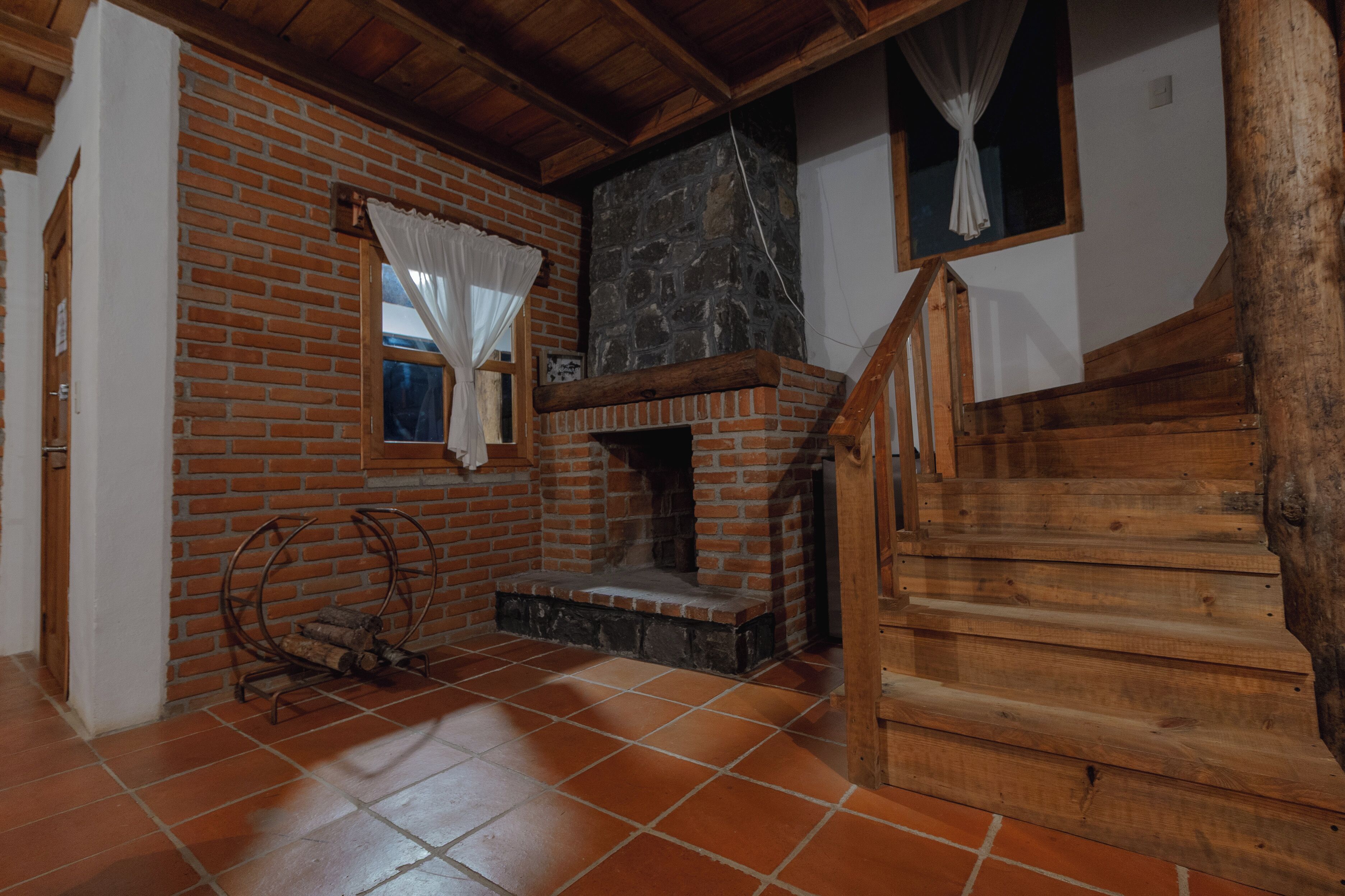Una habitación con chimenea de ladrillo, escalera de madera y suelo de baldosas.
