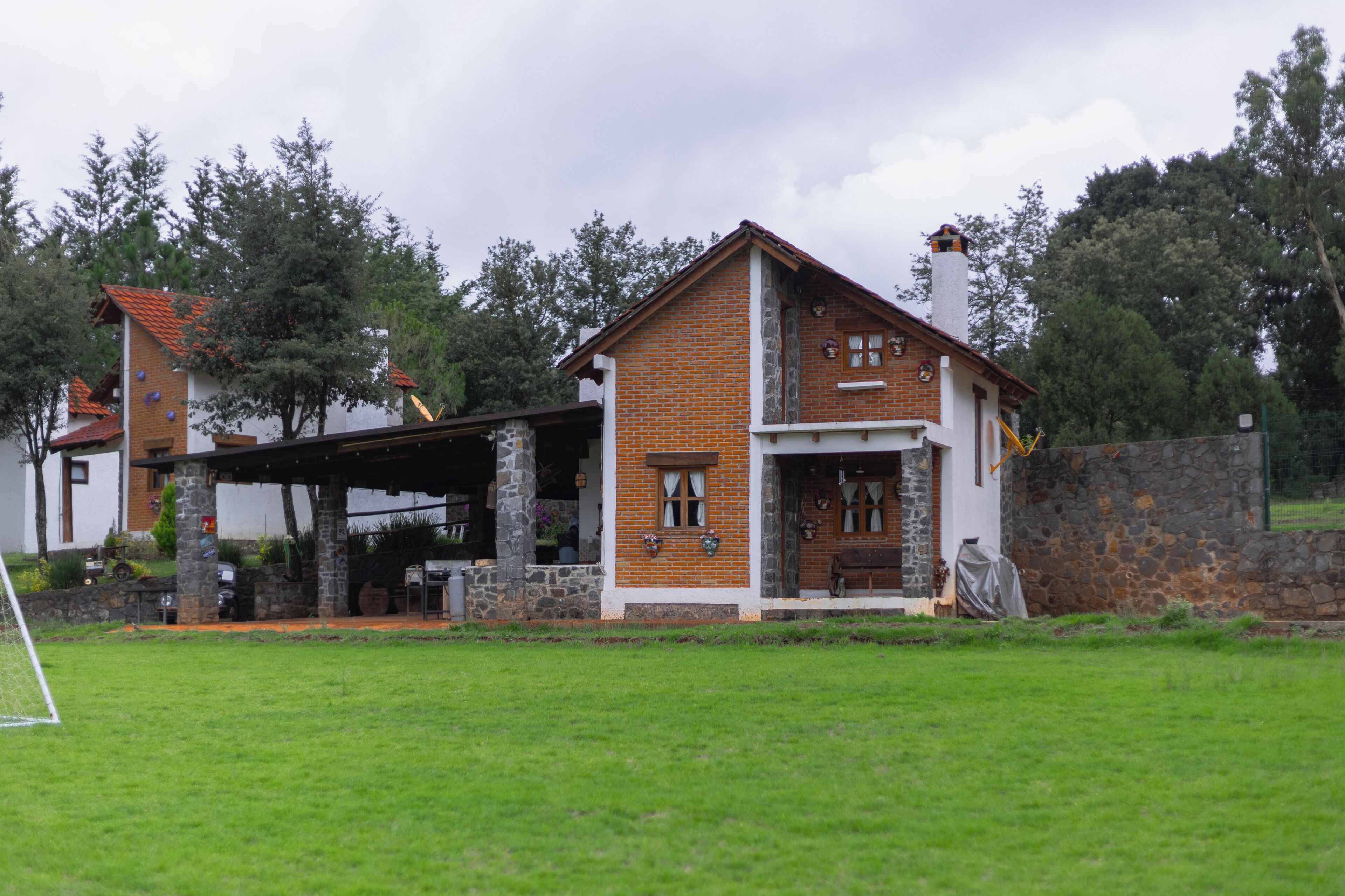 Una casa de dos pisos con fachada de ladrillo, chimenea de piedra y un porche cubierto.