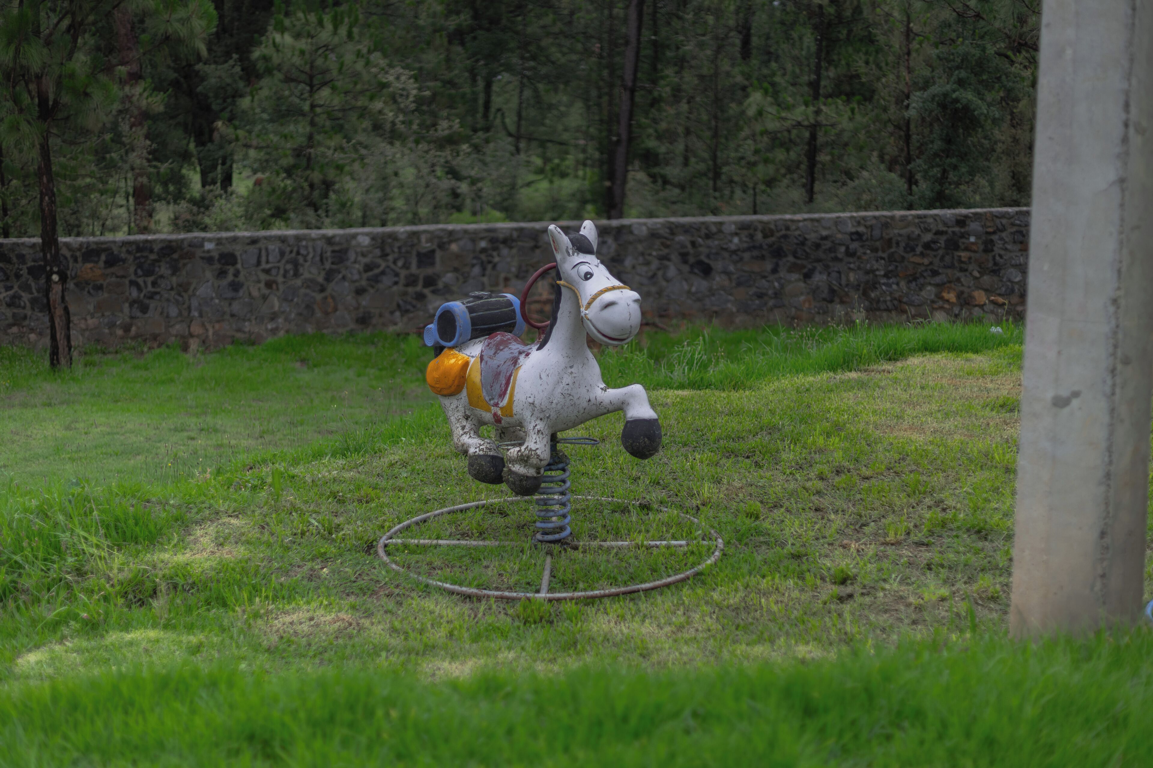 Una escultura de caballo inmóvil en un campo cubierto de hierba, con un muro de piedra al fondo.