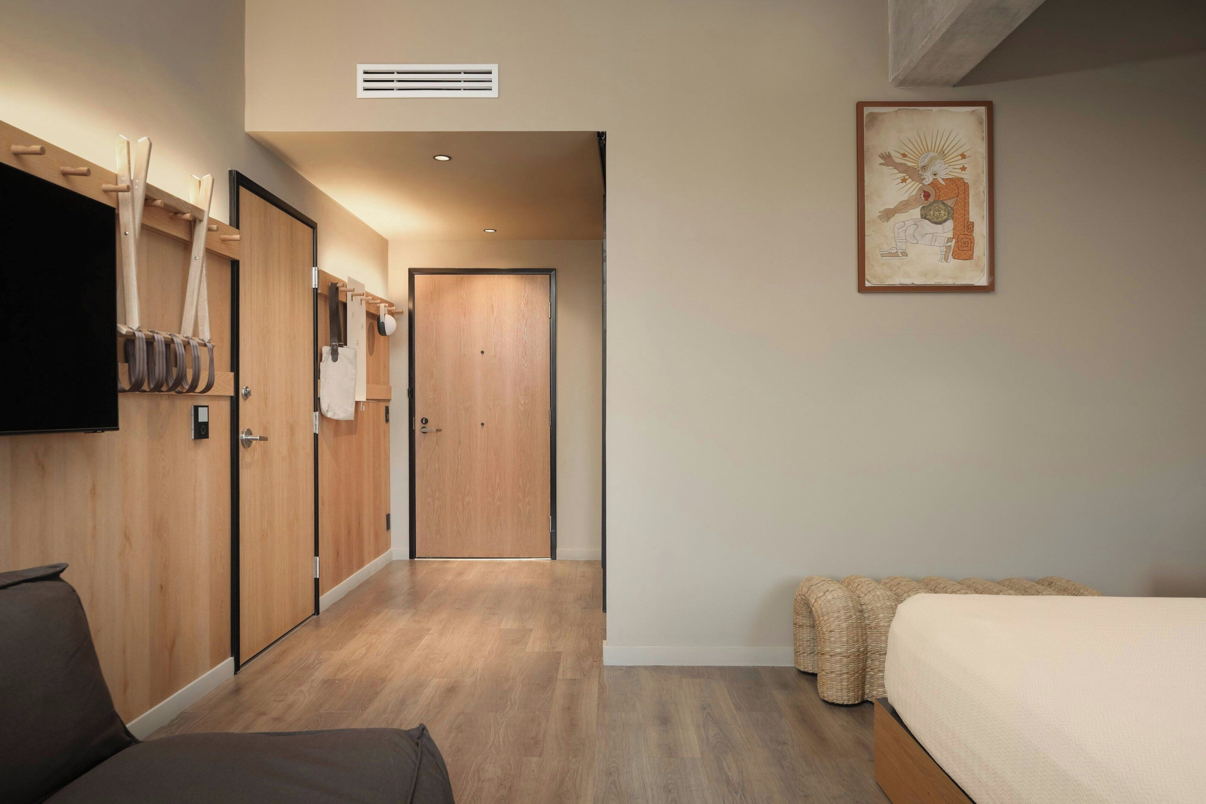 Habitación de hotel con cama, sofá, armario de madera, perchero y un cuadro en la pared.