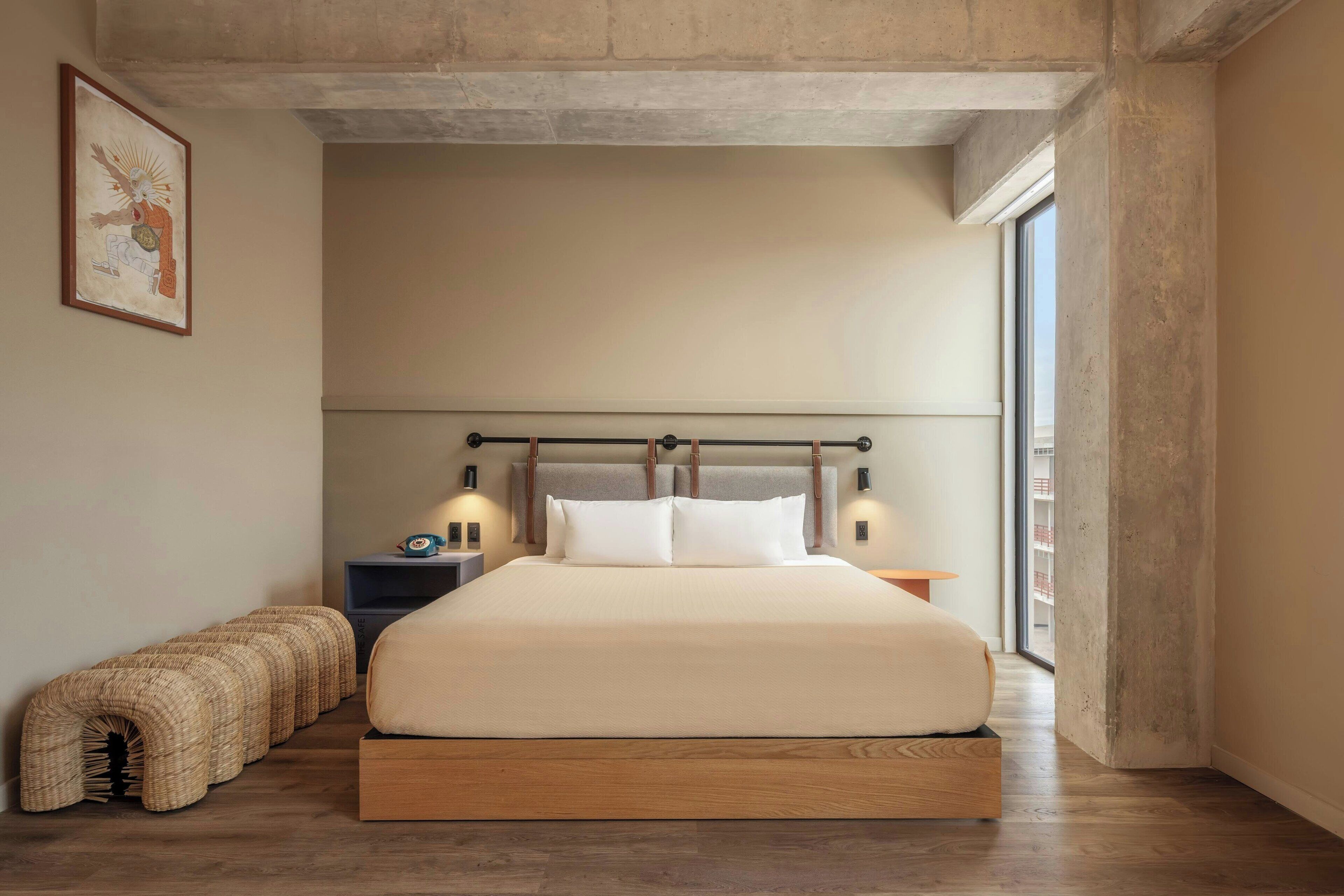 Un dormitorio moderno con una cama grande, mesitas de noche, un banco y un ventanal amplio.