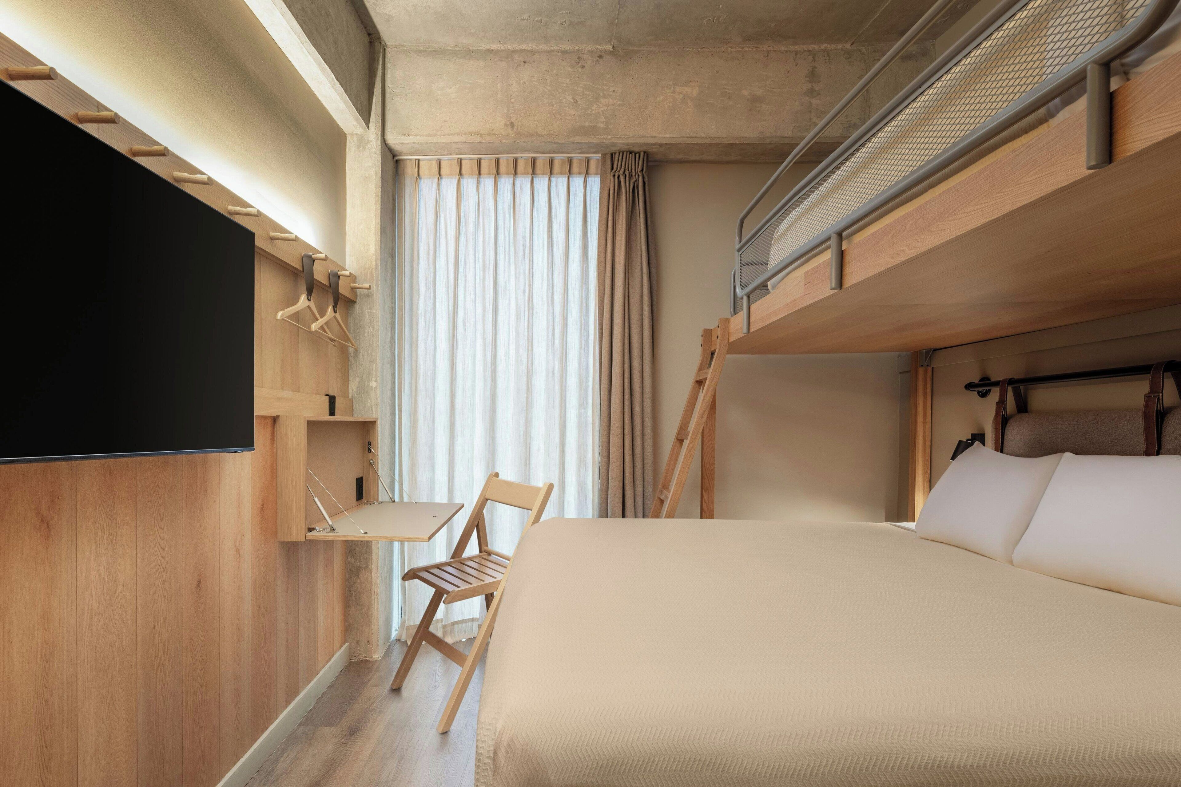 Une chambre avec un lit superposé, un téléviseur à écran plat fixé au mur, un bureau en bois et une chaise.